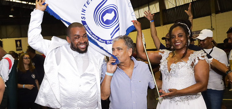 Gilberto Dourado, presidente do SINTETEL, beija a bandeira do SINTETEL conduzida pelo casal da Mocidade Alegre